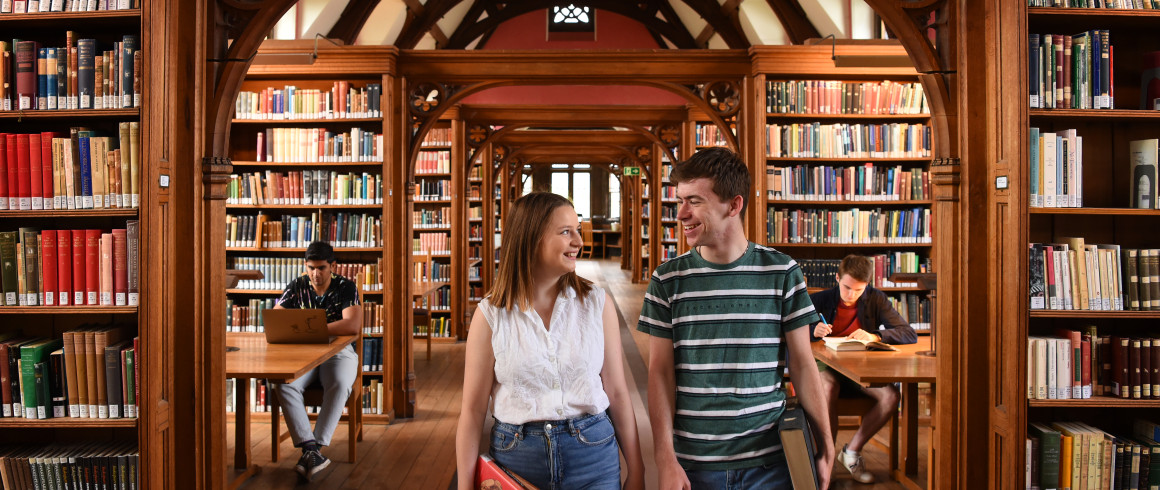 Two students holding books walking through the top floor of Pembroke's library.