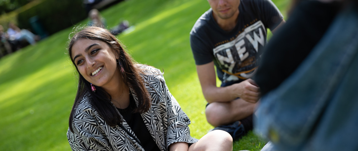 Image of student sitting on grass smiling with her friends